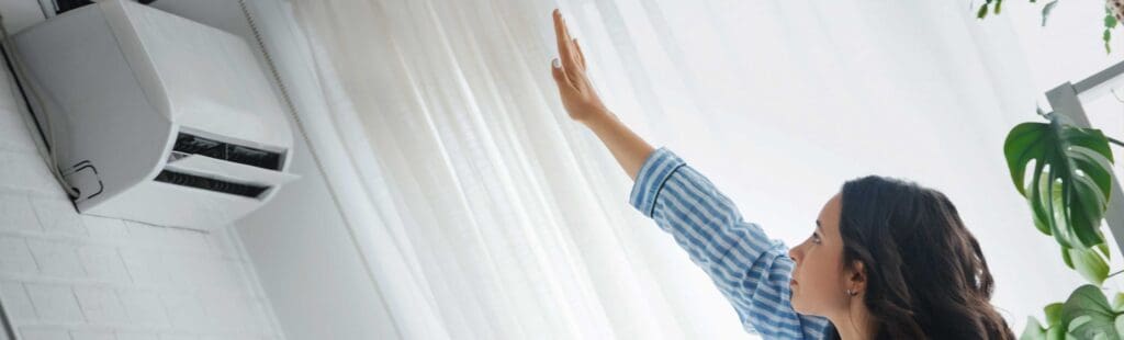 A woman trying to check the cooling of the ductless split AC by placing her hand in front of the Ac vent.